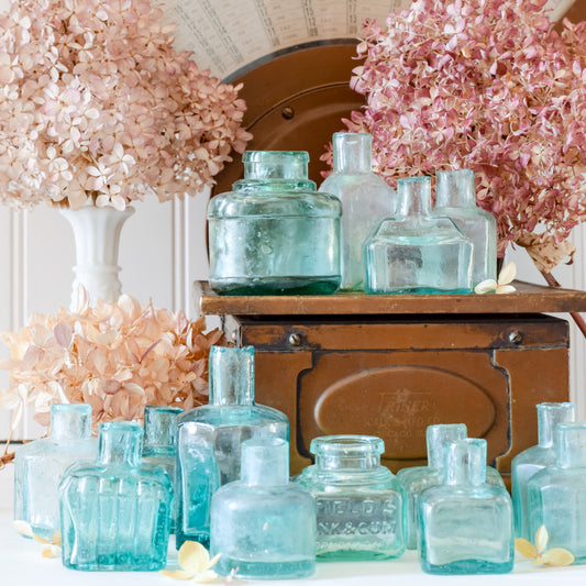 Collection of vintage turquoise bottles with pink floral arrangements on a wooden surface.